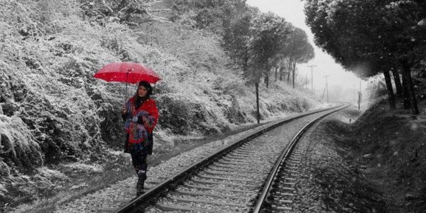 женщина в красном идет вдоль железнодорожных рельс